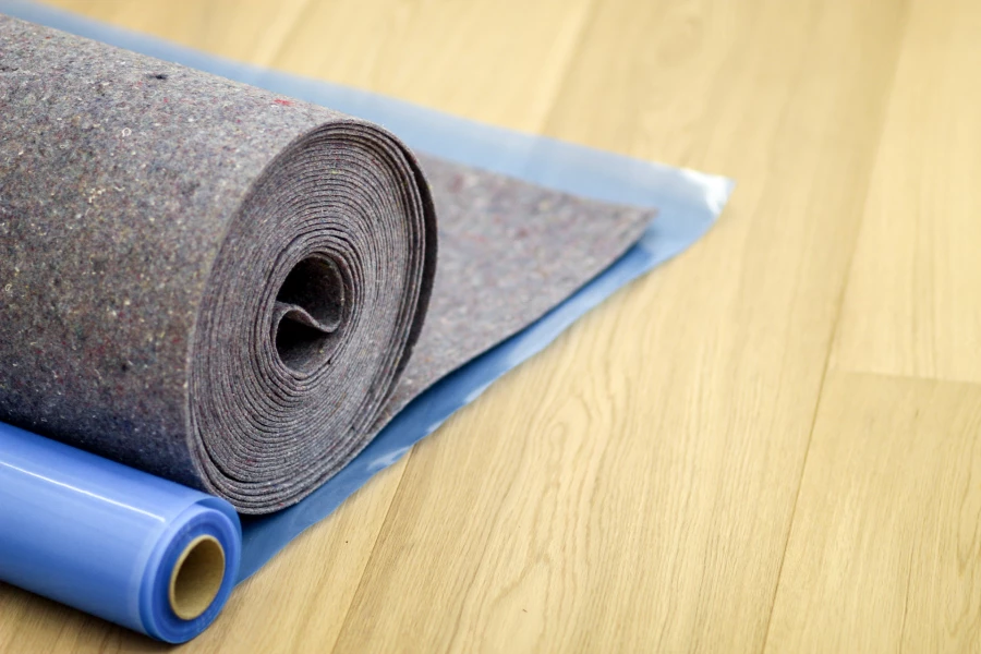 Rollen aus grauem Filz und blauer Folie liegen auf einem hellen Holzboden