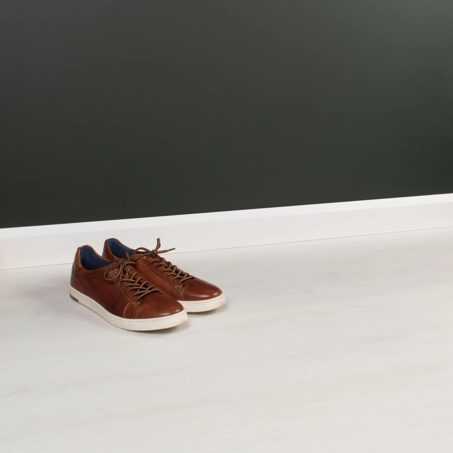 Braune Lederschuhe auf einem sehr hellen Vinylboden vor einer dunkelgrünen Wand