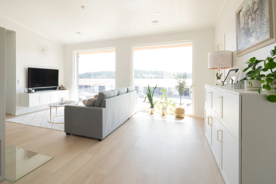 Helles Wohnzimmer mit grauem Sofa, weißen Möbeln und hellem Boden in Eichenoptik (KI-generierte Visualisierung)