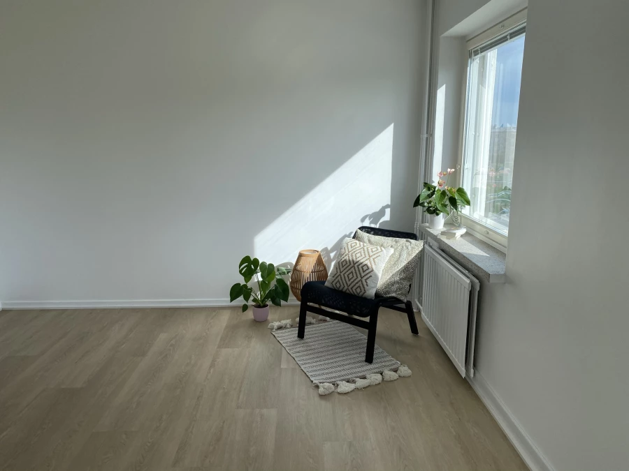 Leerer Raum mit grauen Wänden, Sessel am Fenster und Boden in Eichenoptik (KI-generierte Visualisierung)