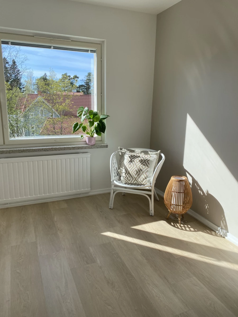 Sonniger Raum mit Rattanstuhl am Fenster und Boden in Eichenoptik